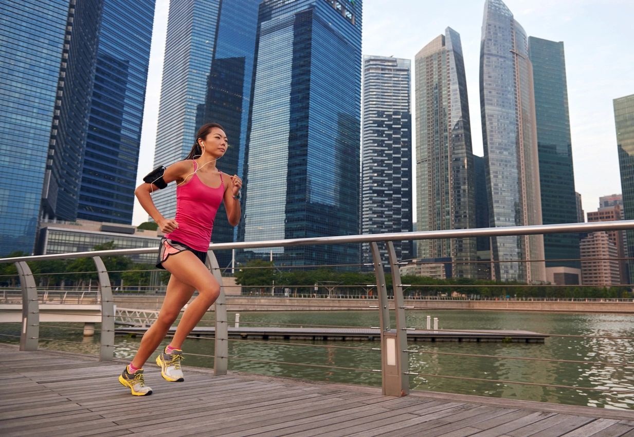 A woman running on the boardwalk in front of tall buildings.